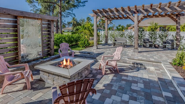An outdoor firepit surrounded by a patio area and rock and pine mulch. Landscaping boulder add an accent to the landscaping.
