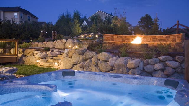 Brilliant Blue hot tub and an awesome fire pit and landscaping in the background surrounded by a boulder retaining wall and a fire pit.