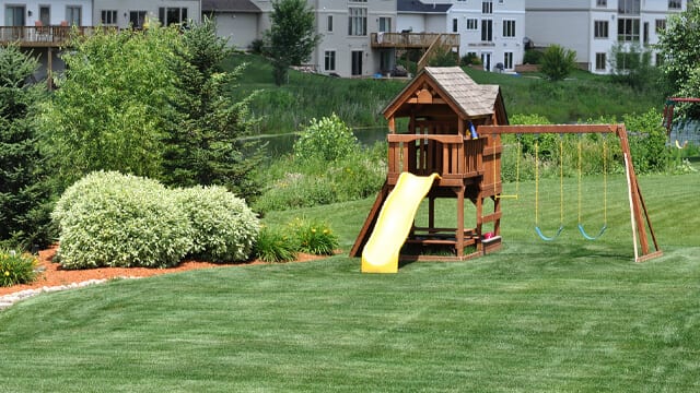 A playground in a suburban backyard surrounded by simple backyard landscaping.